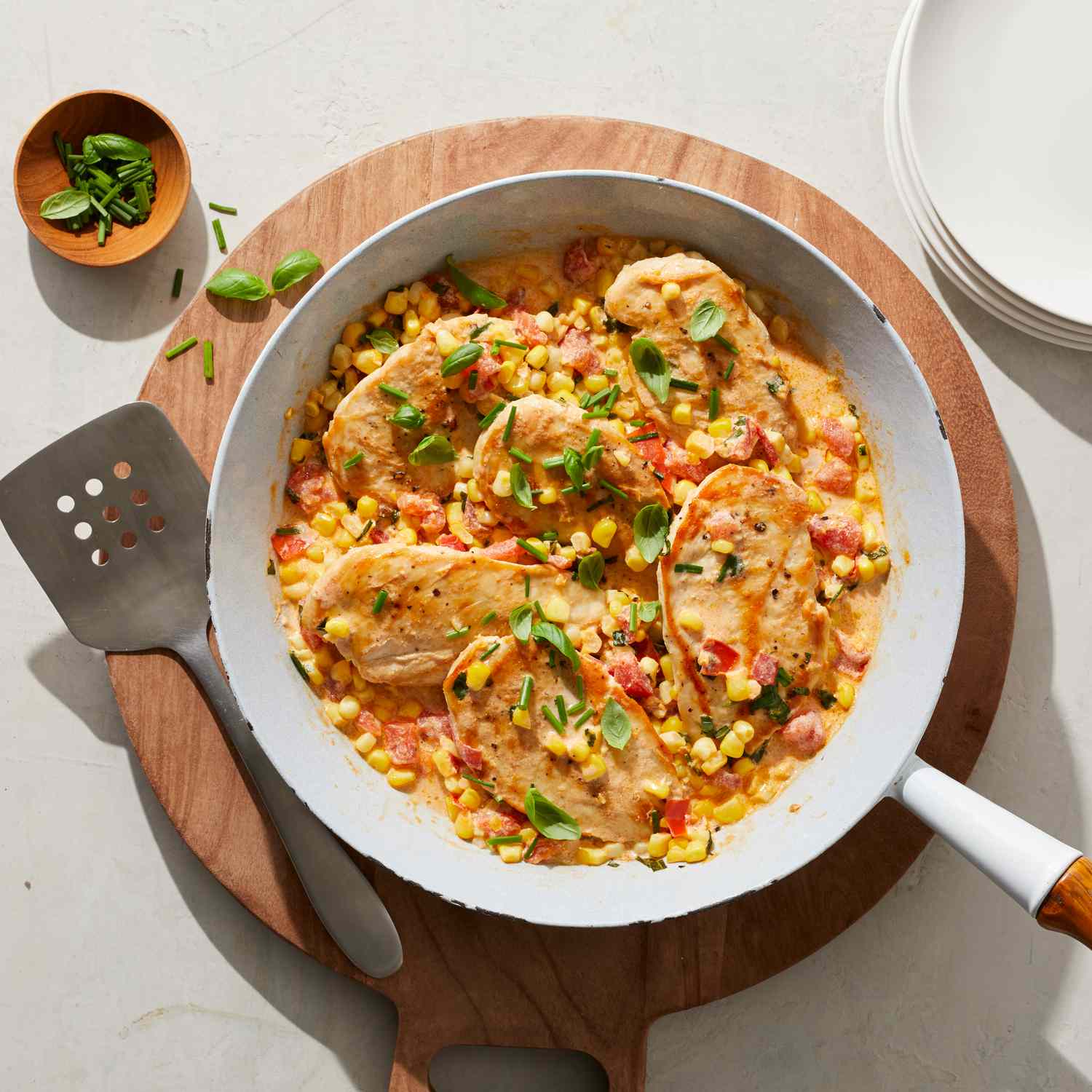 20-minute creamy skillet chicken with corn, tomato & basil in a white sautÃ© pan, placed atop of a round wooden serving board