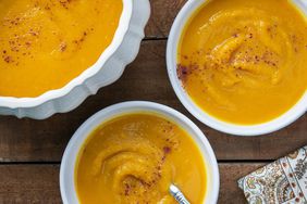 2 bowls of Persian-Style Butternut Squash Soup and a tureen filled with more soup, on a wooden surface.