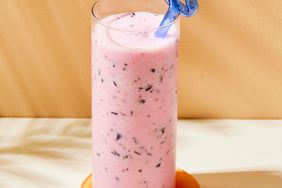 glass of pink smoothie with dark blue specs and a blue straw