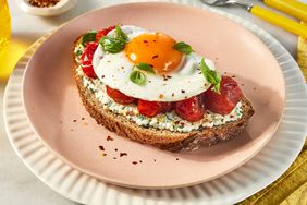 Blistered Cherry Tomato Toast with a Fried Egg on a plate with a small dish of crushed red pepper to the side