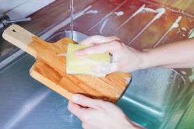 an image showing someone washing a wooden cutting board in the sink