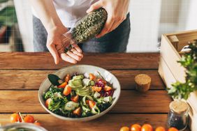 a photo of a person pouring pumpkin seeds into their hand while making a salad