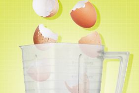 Close up on the opening of a blender with egg shells falling in