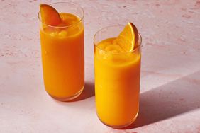 Two tall glasses filled with carrot smoothie, garnished with an orange wedge