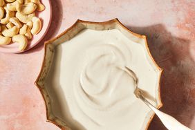 A bowl with cashew cream and a silver spoon, and a bowl of whole cashews in the upper left corner