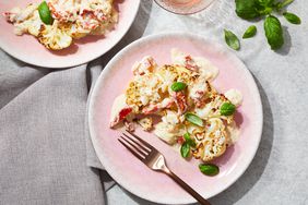 The cauliflower steaks with sun-dried tomato cream sauce recipe, portioned out on two pink plates, and garnished with fresh basil leaves
