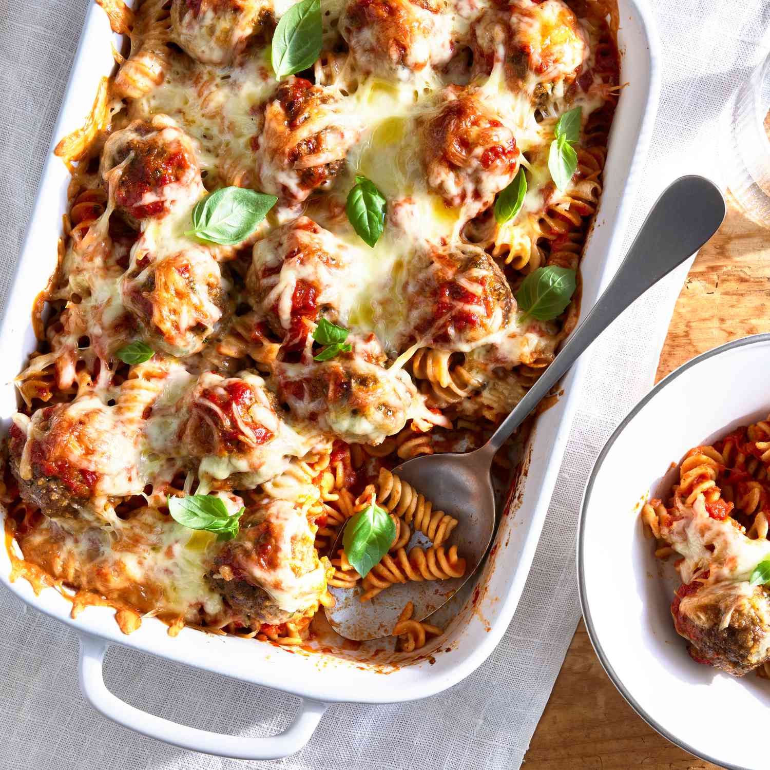 Cheesy meatball casserole baked in a white baking pan, topped with fresh basil