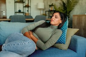 a photo of a woman laying on the couch while holding onto her stomach
