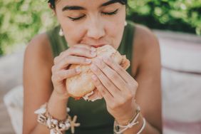 a photo of a woman eating a sandwich outside