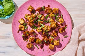 Balsamic Tofu Bites on a pink plate with small blue dish of basil