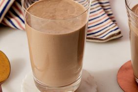 side shot of a light brown smoothie in a tall glass with a striped napkin behind