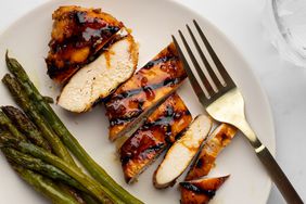 Overhead close up view of sliced Maple-Glazed Chicken Breasts recipe with asparagus on a white serving plate with fork
