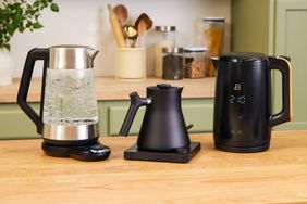 Three electric kettles on top of a butcher block countertop in a kitchen.