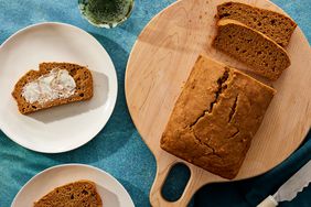 Overhead view of a slice of Maple-Cinnamon Sweet Potato Bread recipe on a white plate and a partially sliced loaf on a wooden cutting board