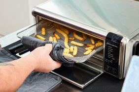 Hand removing a tray of crinkle fries from the Ninja Digital Air Fry Countertop Oven