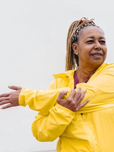 African senior woman doing workout routine while stretching outdoor - Focus on face