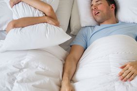 man and woman in bed - woman covering her face with pillow, man calmly sleeping