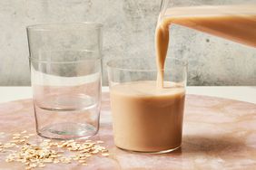 Homemade oat milk getting poured from a pitcher into a clear drinking glass