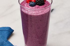 Mixed-berry breakfast smoothie recipe in a tall glass, topped with fresh raspberries, blueberries and one blackberry