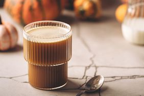 a photo of a glass of pumpkin latte with pumpkins in the background
