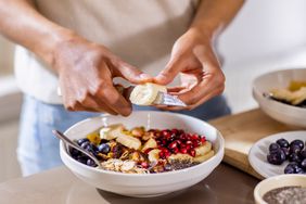 a photo of a person slicing up bananas for their bowl of yogurt