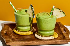 Two glasses filled with pineapple spinach smoothie, garnished with a pineapple wedge and a green and white striped straw