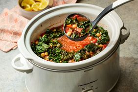 The slow-cooker mediterranean diet stew in a slow cooker, with a serving spoon holding some of the soup up above the slow cooker