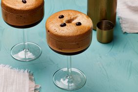 Two soufflÃ© espresso martinis in tall round martini glasses on a turquoise background