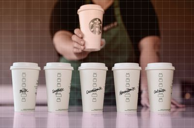 a photo of various milks in Starbucks coffee cups and a barista behind them