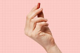 a photo of a hand holding up a red supplement capsule