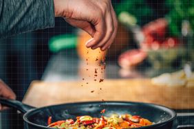 a photo of a person sprinkling a spice onto vegetables cooking in a pan