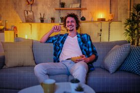 a photo of a man eating a snack on the couch at night while watching television
