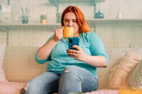 a photo of a woman sipping tea while sitting on the couch and looking at her phone