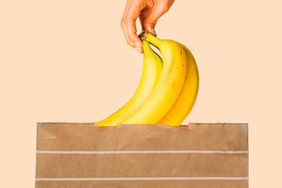A hand placing a bunch of bananas in a paper grocery bag