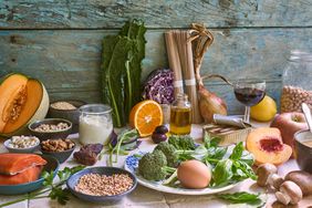 a selection of whole fruits, vegetables, whole grains and other whole foods laid out on a wooden surface