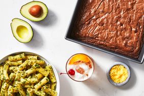 pesto noodles, brownies, an avocado, infused salts, and a whisky sour on a white marble surface