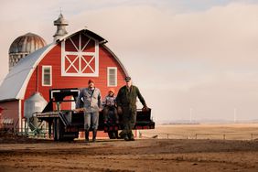 two men and a child standing infront of a barn