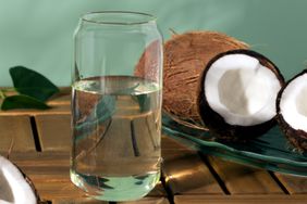 a photo of coconut water in a glass and coconut in the background