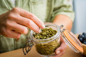 a photo of a hand grabbing pumpkin seeds from a jar
